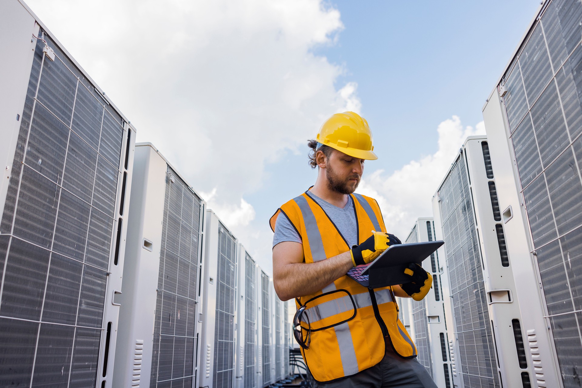 Using a portable computer, blue collar worker checks air conditioning system.
